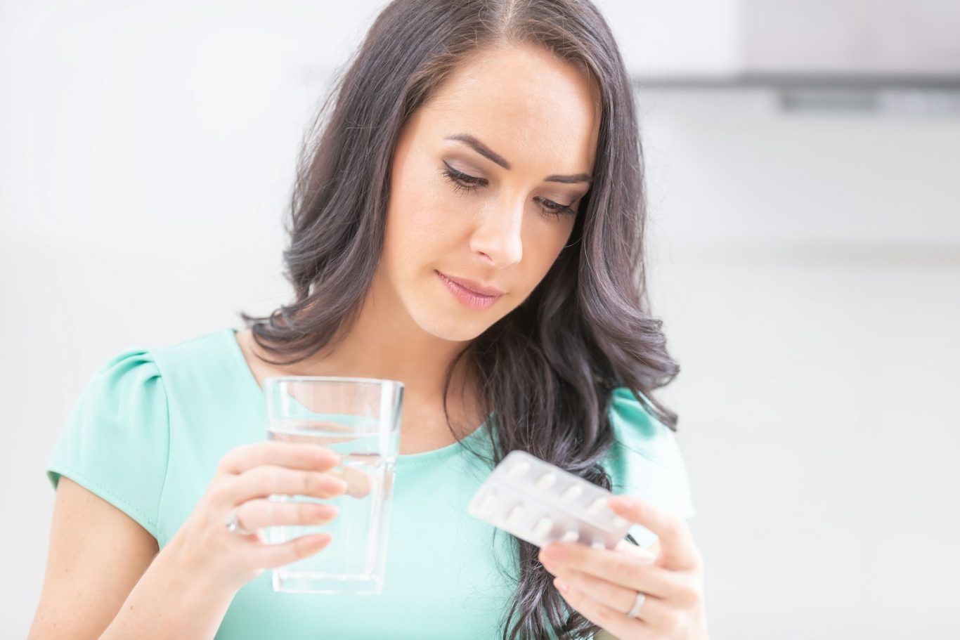 Serialization protects patients Woman holding a glass of water and a blister pack of pills, appearing contemplative.